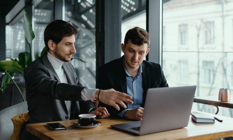 Two businessmen pointing laptop screen while discussing